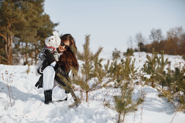 家庭在冬季公园散步的可爱女孩穿着棕色夹克的女人牵着狗的女人冬天白色肖像