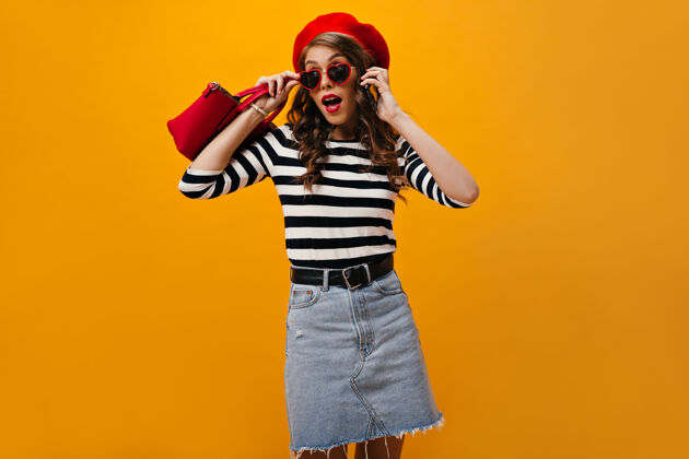 帽子一个戴着红色贝雷帽的女人摘下太阳镜打电话的镜头一个卷发的现代女孩穿着条纹衬衫 手提袋摆姿势太阳镜休闲牛仔裙