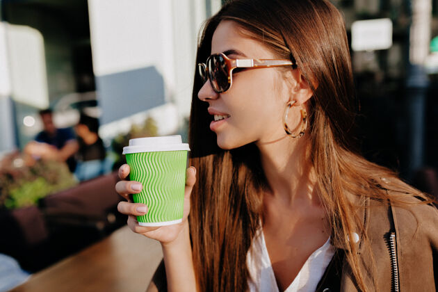 女人在城市背景上 一位戴着眼镜 喝着咖啡脚的快乐白人妇女的特写肖像散步时尚休闲