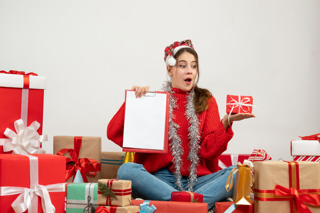 节日前视图可爱的圣诞女孩与圣诞帽举行礼物和文件坐在周围的礼物圣诞老人礼物文件