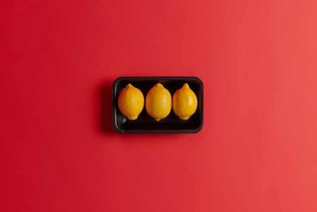 活力三个全黄酸甜可口的柠檬放在黑色的盘子里 在红色的工作室背景上隔离开来富含维生素c的天然产品健康的营养理念有机新鲜柑橘类水果顶视图收获酸味有机