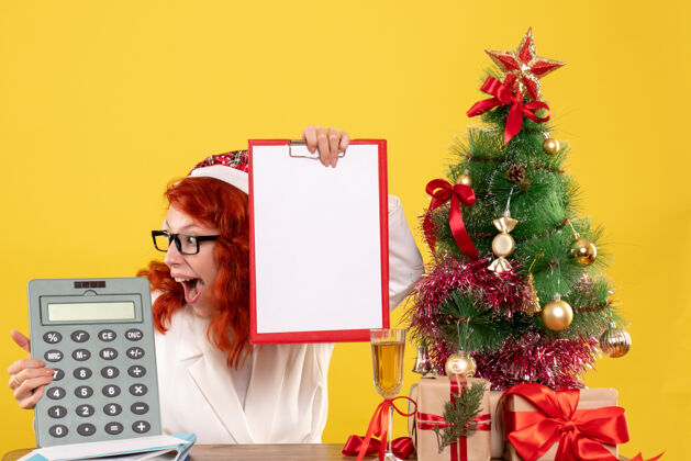 圣诞树前视图女医生拿着计算器围着圣诞礼物和圣诞树颜色礼物年