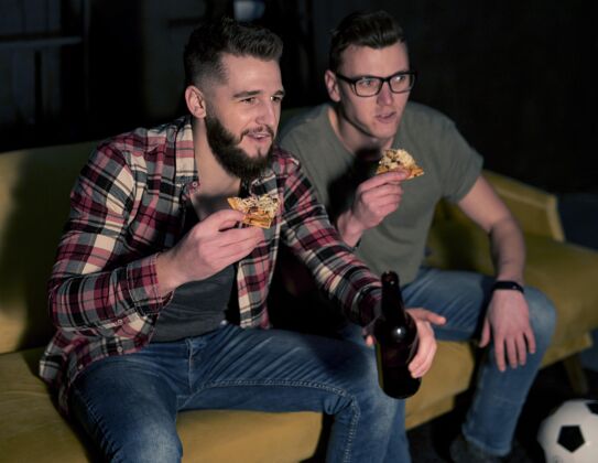 水平男性朋友一边看电视上的体育节目 一边喝着啤酒和披萨体育电视同志