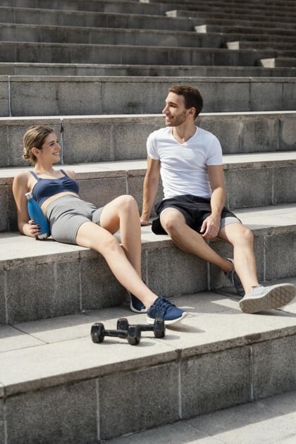 活力微笑的女人和男人在台阶上休息 同时锻炼活泼楼梯健身