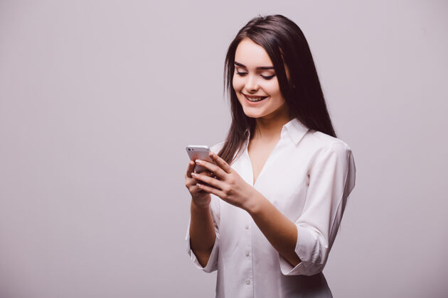 短信一个微笑迷人的女人在手机上发短信的肖像 而孤立地站在白色背景上沟通女性人