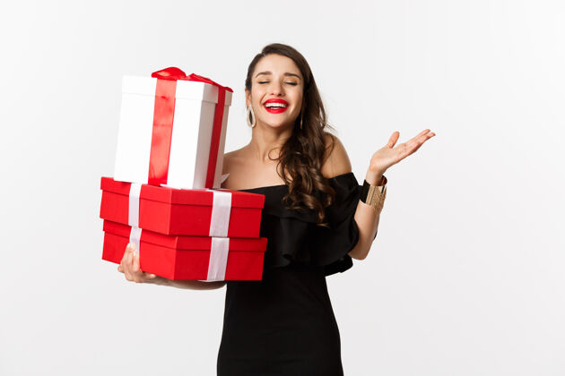美容庆祝和圣诞假期的概念兴奋和快乐的女人收到礼物 拿着圣诞礼物和喜悦 站在白色背景的黑色礼服唇膏模特表情