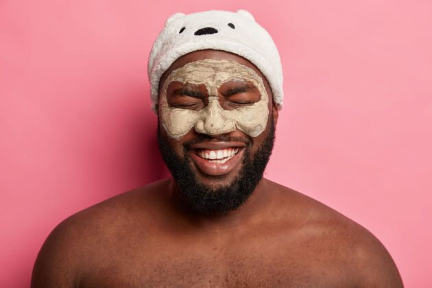 胡须美国黑人戴着泥面具 表达积极情绪面部护理过程清洁