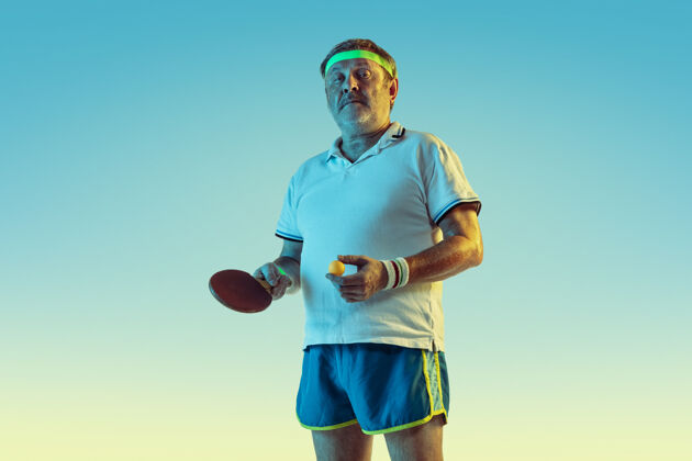 发球资深男子在霓虹灯下的斜坡墙上打乒乓球身材魁梧的白种人男模保持活跃 运动运动 活动 运动 幸福 健康的生活方式的概念球微笑装备