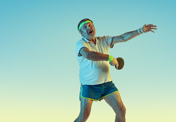 装备资深男子在霓虹灯下的斜坡墙上打乒乓球身材魁梧的白种人男模保持活跃 运动运动 活动 运动 幸福 健康的生活方式的概念活跃老年人球员