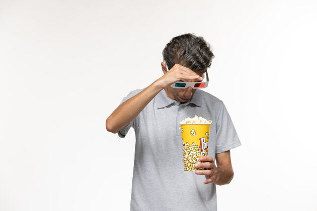 电影院正面图：戴着d型太阳镜的年轻男性手持爆米花站在白色的地面上电影球衣男