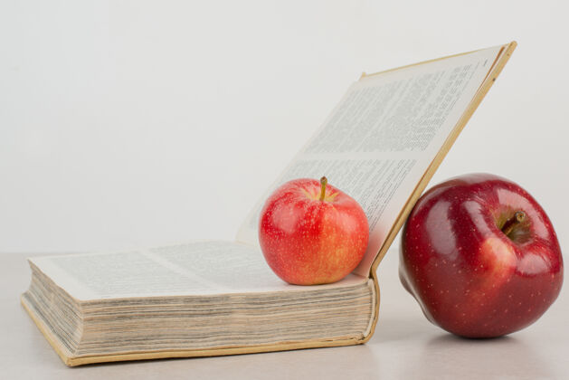 翻页白桌子上有两个带书的新鲜苹果红色水果苹果