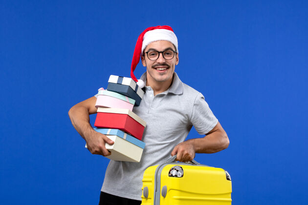 专业前视图年轻男性手持礼物和包在蓝色背景飞机上度假工业工作圣诞节