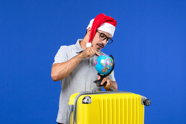 男性正面图年轻男子背着黄包带着地球仪在蓝墙飞机上度假旅行人运动飞机