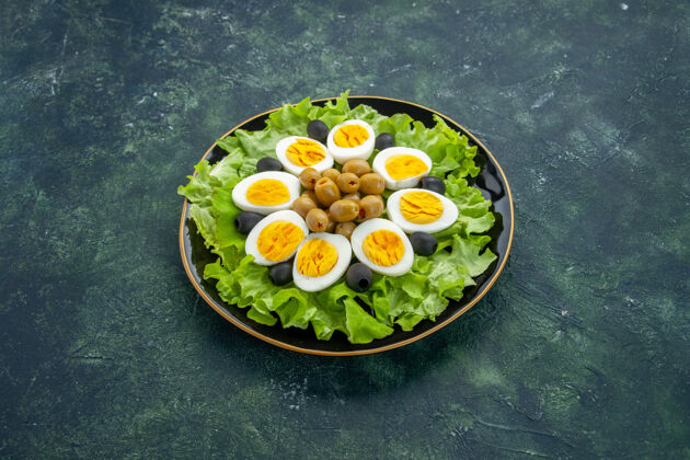 晚餐前视图煮熟切片鸡蛋与橄榄和绿色沙拉在深蓝色的背景盘子绿色景观