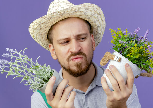 迷茫特写镜头中困惑年轻英俊的斯拉夫园丁身穿制服 戴着帽子 看着紫色墙上孤立的花盆风景特写帽子