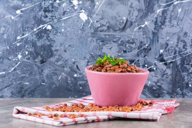 食物粉红色的煮豆子碗 大理石表面铺桌布欧芹盐胡椒粉