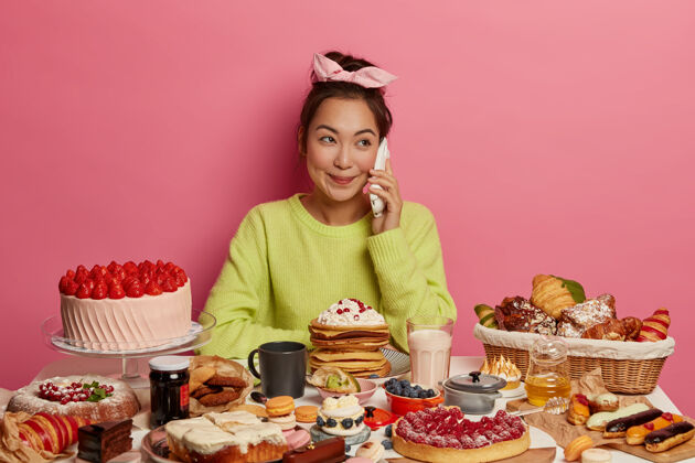 讲话相当积极的韩国女性有愉快的电话交谈 甜食和蛋糕 吃可口的零食 宠爱自己 孤立的粉红色背景美味房子跳伞