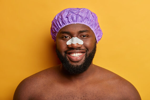 浴室帅气的黑皮肤男人用鼻子贴片来减少黑点和皱纹 戴着浴帽面部清洁和护理概念面部微笑姿势