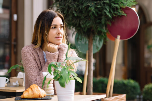 脸美丽的女人穿着暖和的毛衣坐在自助餐厅里等着别人她在一旁看她用一杯热饮取暖秋天的日子 外面的肖像 会议漂亮工作人