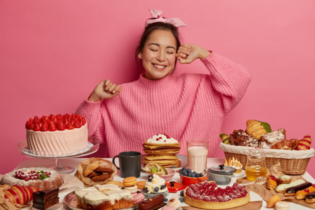 伸展快乐的亚洲生日女孩来参加茶话会 吃着香甜可口的蛋糕 周围有许多甜点 在粉红色的背景下摆姿势牛角包烘焙享受