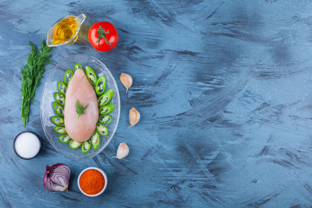 有机把鸡胸肉和辣椒片放在玻璃盘子里 旁边放着香料 油和各种蔬菜 放在蓝色的桌子上平铺油食物