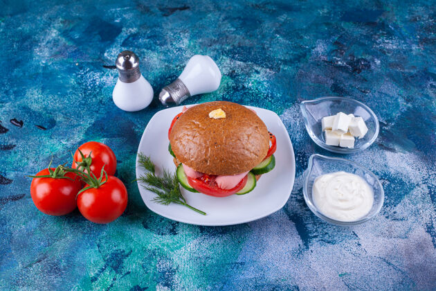胡椒白色盘子里放着美味的汉堡包和西红柿 放在蓝色的表面上食物汉堡面包