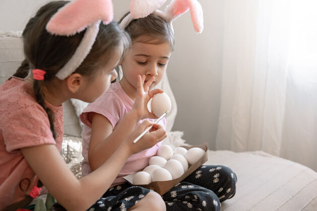 创意小妹妹们在家里的沙发上画复活节彩蛋装饰兔子女孩