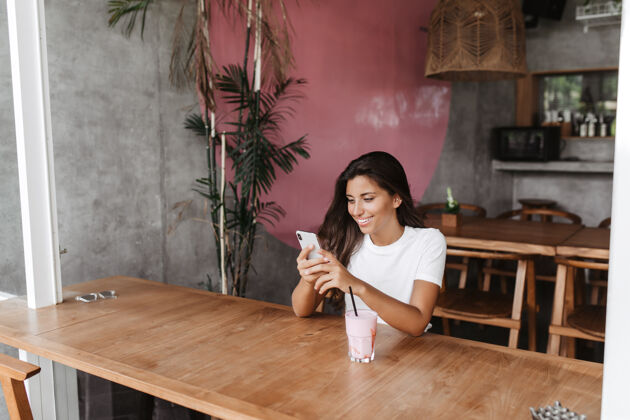 咖啡馆坐在咖啡馆里用智能手机微笑聊天的女人的画像深色头发奶昔女性