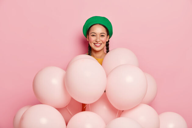 胭脂好看的亚洲女模特戴着绿色贝雷帽 站在许多气球旁边 在粉色背景上摆姿势 庆祝生日事件时尚女人