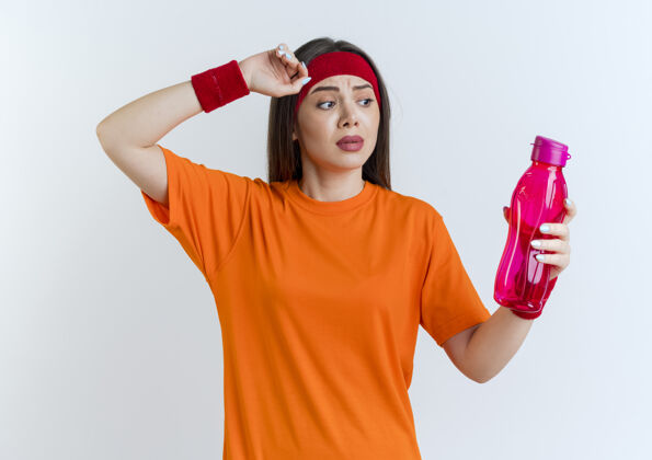 水印象深刻的年轻运动女子戴着头带和腕带拿着水瓶摸头运动瓶子运动