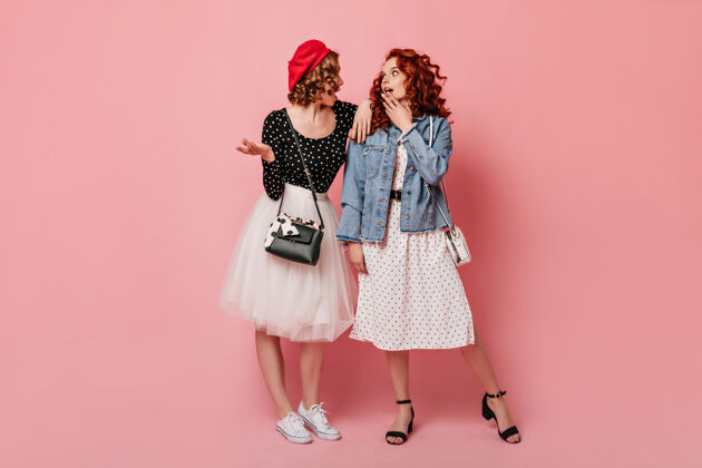 时尚两位时尚女孩在粉色背景下交谈的全幅照片优雅女士的摄影棚拍摄优雅裙子粉色背景