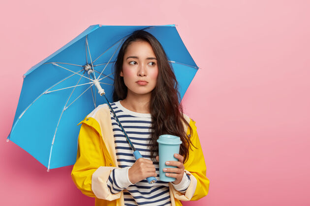 隐藏悲伤的女人在阴雨天感到沮丧 有季节性抑郁 在防水伞下摆姿势 穿条纹套头衫和雨衣年轻杯子防水