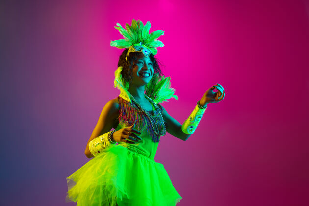 模型舞蹈嘉年华中美丽的年轻女子 霓虹灯下羽毛在渐变墙上翩翩起舞的时尚化装服装节日庆典 节日时间 舞蹈 派对 娱乐的概念特内里费面具女性