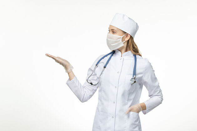 制服正面图女医生身穿医疗服戴口罩因冠状病毒对淡白色壁病冠状病毒-大流行性病毒病到期套装佩戴