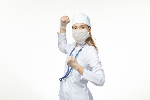 医生正面图：穿着白色医疗服 戴着白色口罩的女医生 在浅白的墙壁上保护自己免受冠状病毒的侵害医疗灯光冠状病毒防护