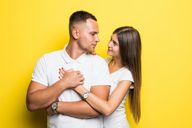 在一起一对身着白色t恤的幸福年轻夫妇在黄色背景上拥抱欢呼站在一起
