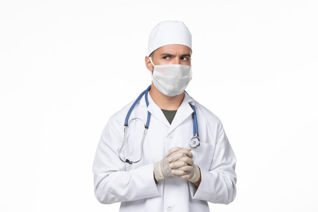 面罩正面图：男医生穿着医疗服 戴着口罩 因为白色光壁上有冠状病毒-大流行性病毒病男人医生疾病