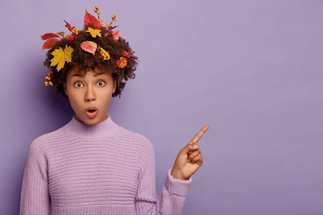 木僵惊讶的黑皮肤女人的肖像点在复制空间 张开嘴 有秋天的叶子和浆果粘在头发上 站在无语和印象深刻 穿着针织紫色毛衣时尚紫罗兰兴奋