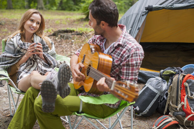 茶杯一对浪漫的情侣在露营男人在弹吉他微笑聚会远足