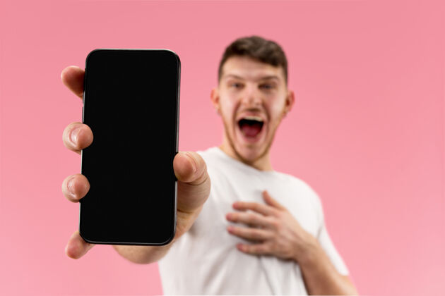 惊奇年轻帅哥在粉色空间展示智能手机屏幕 一脸惊喜惊讶脸胡须