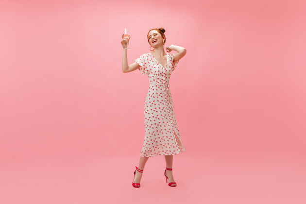 微笑穿着白色樱桃裙的酷女人在粉色背景上吹五彩纸屑乐趣五彩纸屑化妆品