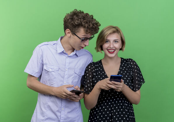 手机一对年轻漂亮的情侣站在绿墙上偷看女友的手机间谍情侣偷窥