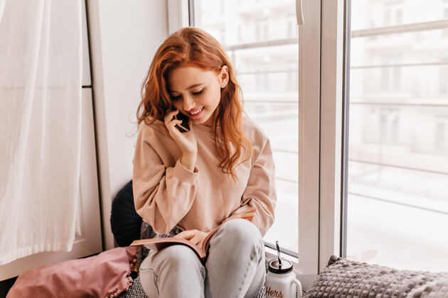黑发浪漫的红发女孩在窗边看书害羞的欧洲年轻女子在打电话年轻女子交谈房子