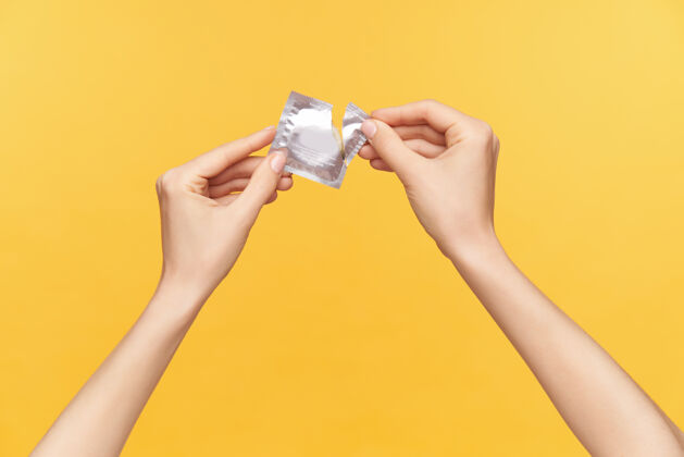 黄色照片中年轻女性举起双手 手上拿着装有避孕套的银包 在橙色背景下被隔离 打开包装关系和性观念手势手指性别