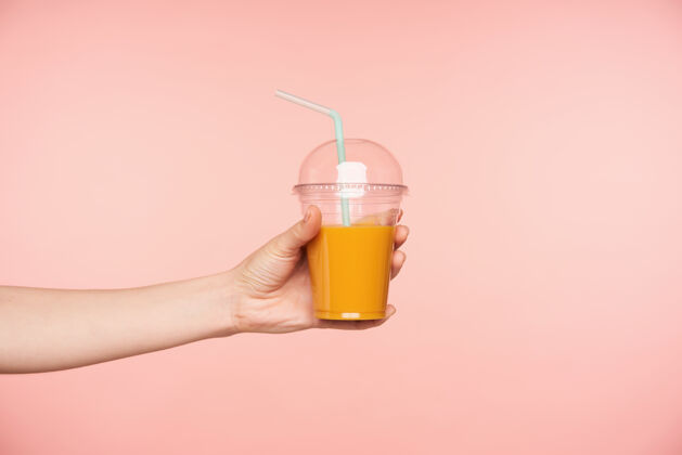 饮料侧视图年轻女子的手被提出 而持有新鲜果汁与吸管在它 孤立的粉红色背景食品和饮料摄影概念身体复制空间特写