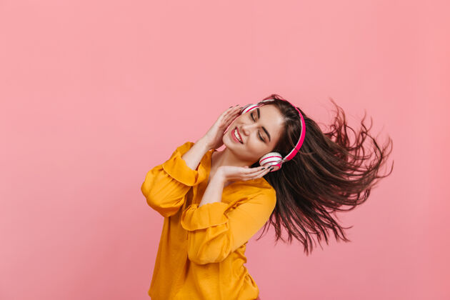 音乐可爱的女孩戴着白色和粉色的耳机积极地在粉色的墙上跳舞 动着长长的头发欢呼年轻梯子