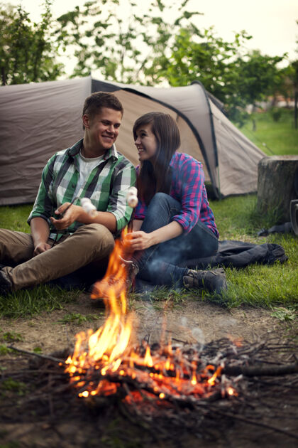 农村场景坐在篝火旁烤棉花糖的年轻夫妇年轻人友谊春天