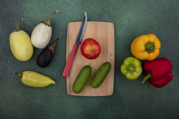 餐用刀在砧板上切黄瓜的西红柿和绿色背景上的彩色甜椒茄子午餐黄瓜茄子