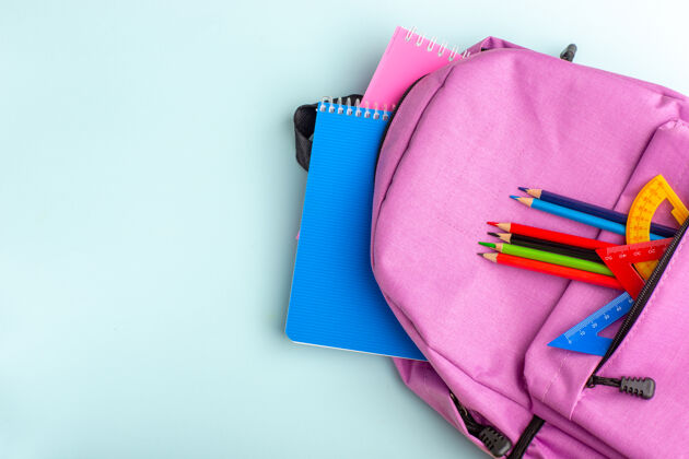 书桌顶视图紫色书包 蓝色书桌上有抄写本和铅笔孩子容器礼物