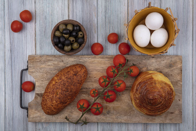橄榄木制厨房板上面包的俯视图 灰色木制背景上有葡萄藤 西红柿 橄榄和鸡蛋传统中国菜西红柿